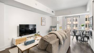 Een moderne woonkamer met een grote flatscreen televisie, een bank, een salontafel en een eethoek met een ronde tafel en stoelen.