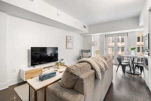 Een moderne woonkamer met een grote flatscreen televisie, een bank, een salontafel en een eethoek met een ronde tafel en stoelen.