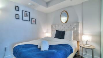 A bedroom with a large bed, a round mirror, and framed pictures on the wall.