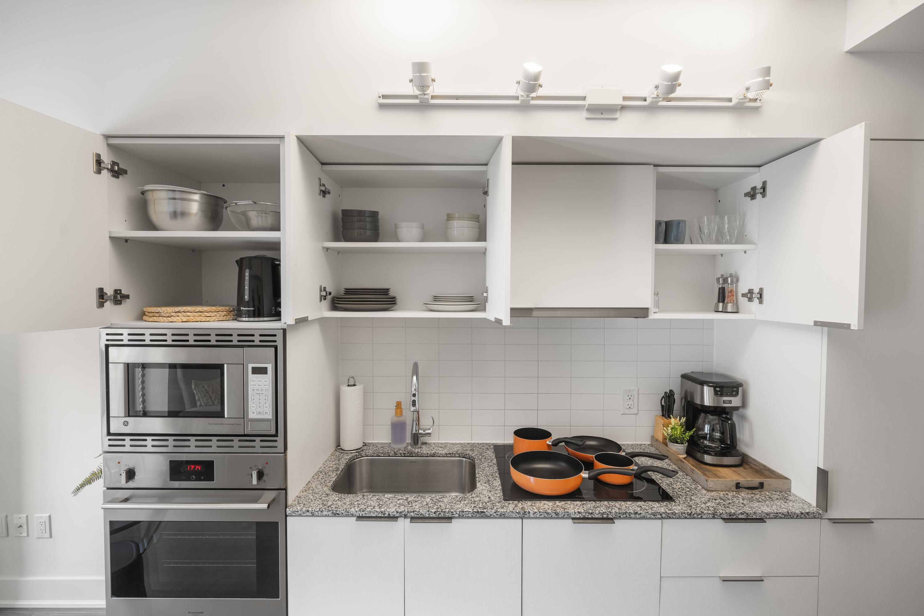 A modern kitchen with white cabinets, a built-in oven, a microwave, and a coffee maker.