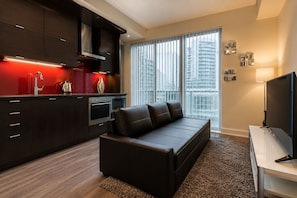 A modern living space with a kitchen, a sofa, a TV, and a city view through large windows. - Chic Suites in Downtown Toronto (Toronto)