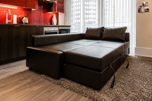 A modern living room with a sectional sofa, a kitchen area with red cabinetry, and a city view through large windows. - Chic Suites in Downtown Toronto (Toronto)