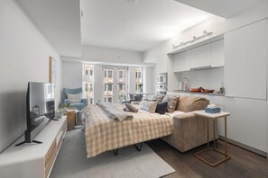 Un dormitorio moderno con cama, mesita de noche, televisor y una pequeña kitchenette.