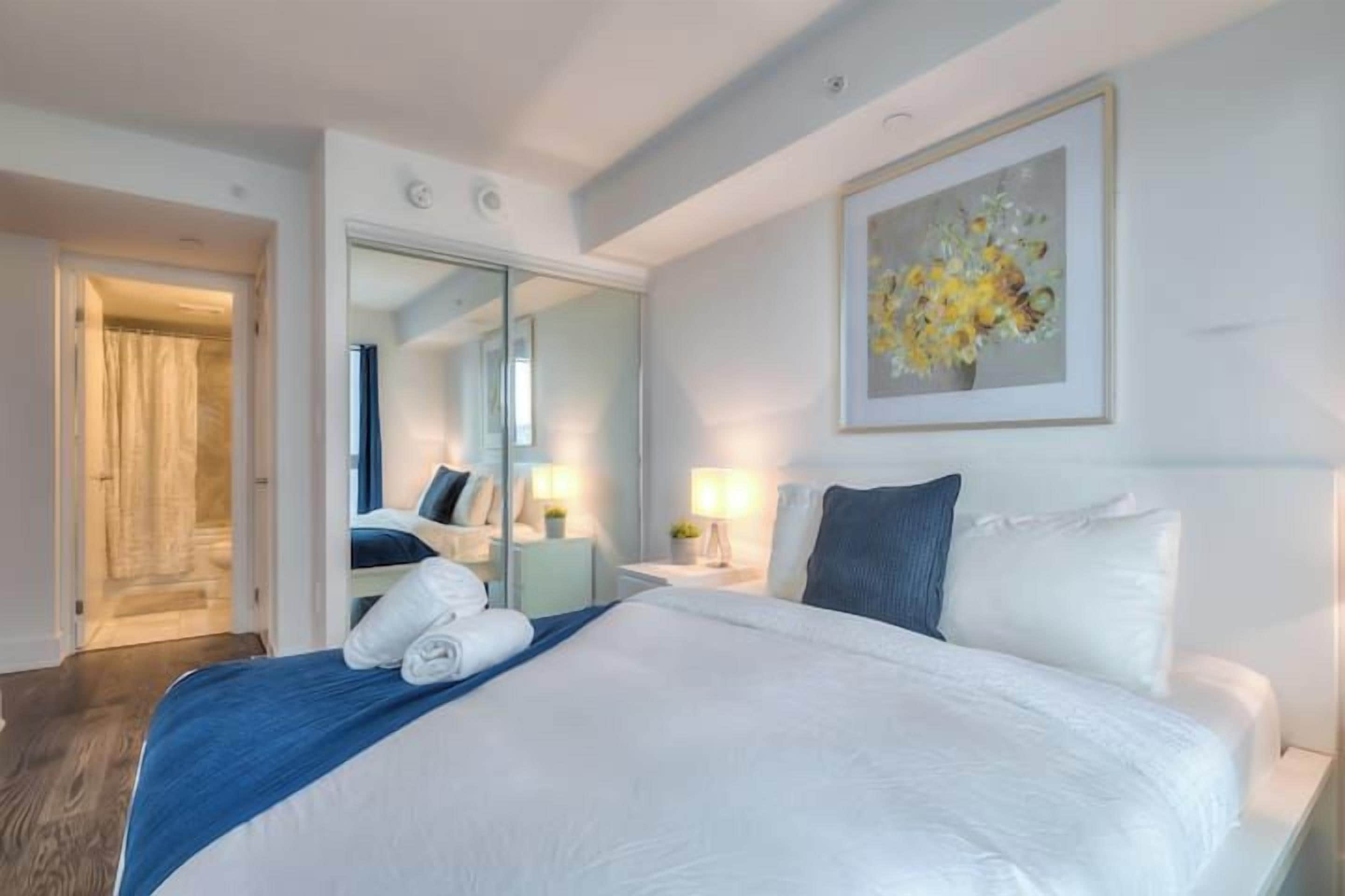 A hotel room with a large bed, a mirror, a painting, and a bathroom visible through an open door.