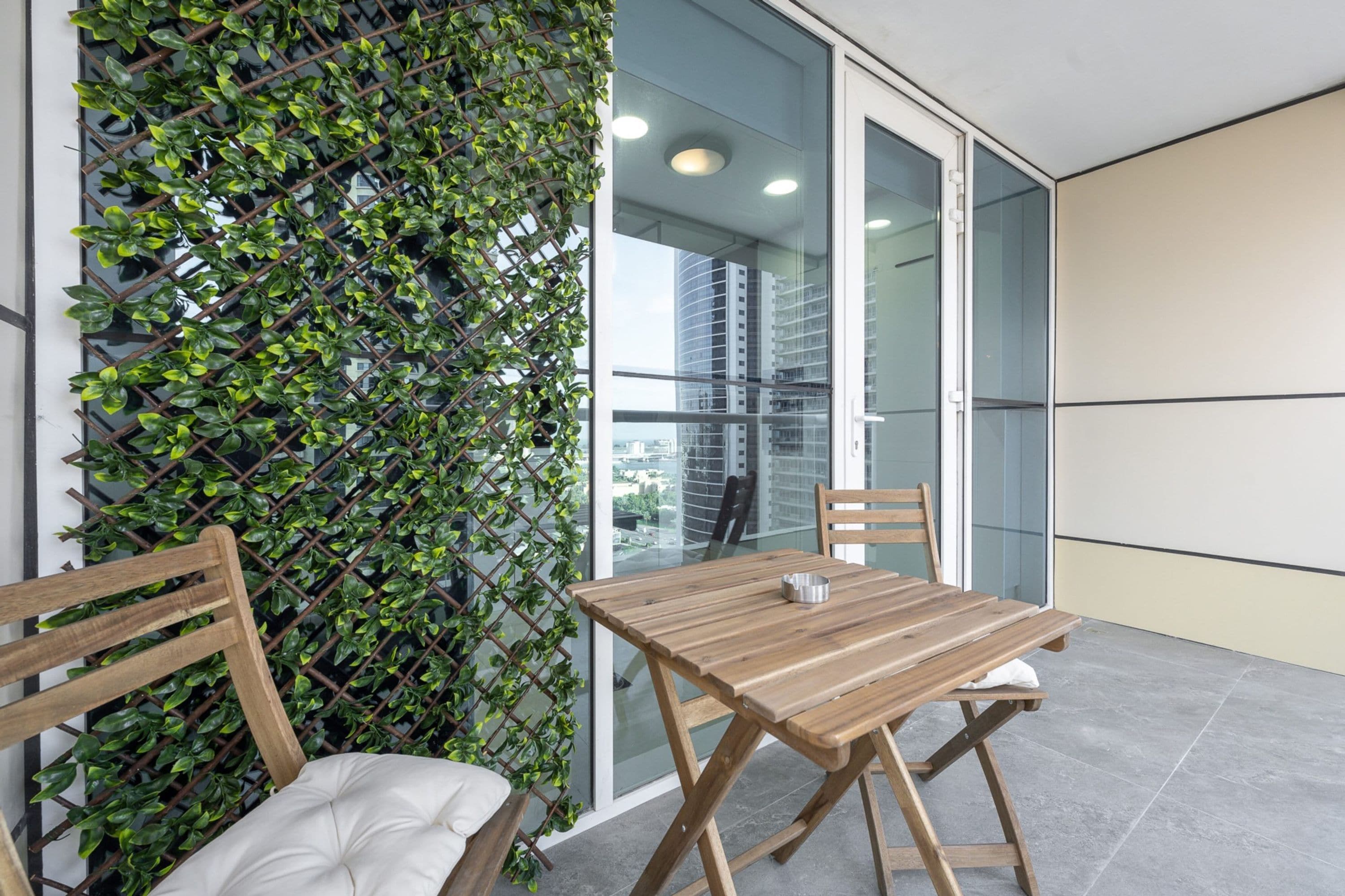 A modern outdoor seating area with a wooden table and chairs, a cushioned bench, and a green climbing plant wall.