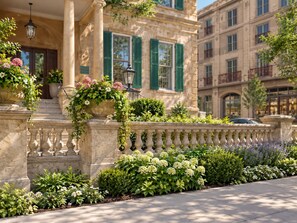 A stone building with a balcony, green shutters, and a flower bed with white flowers. - Sabal House (Savannah)