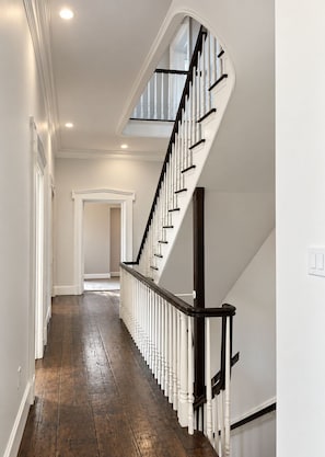 A hallway with a wooden floor, white walls, and a black and white staircase with a skylight above. - Sabal House (Savannah)