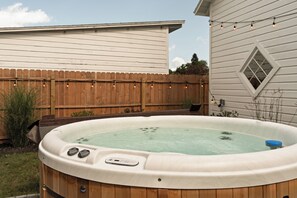 A hot tub in a backyard with a wooden fence and a house in the background.