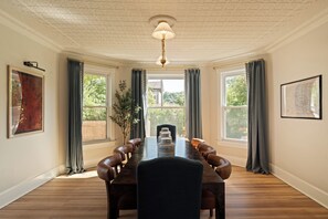 Comedor con una mesa larga, sillas de cuero y ventanas grandes con cortinas.