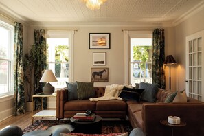 A cozy living room with a brown leather sofa, a small side table with a lamp, and a coffee table with books.