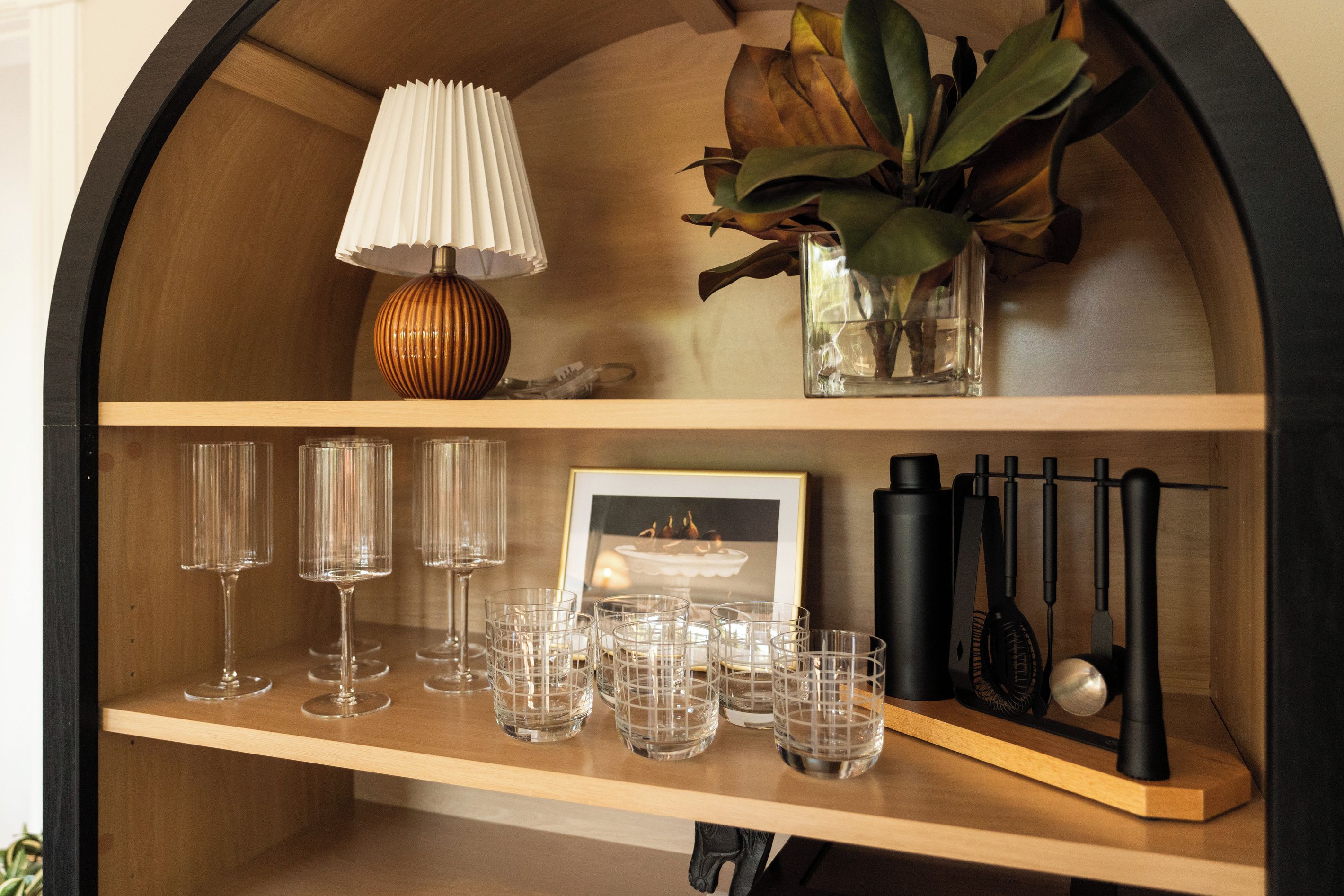 A wooden shelf with a lamp, a vase with a plant, and several glasses.