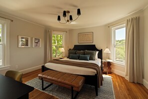 A bedroom with a bed, a bench, a nightstand, a lamp, and a window with curtains.