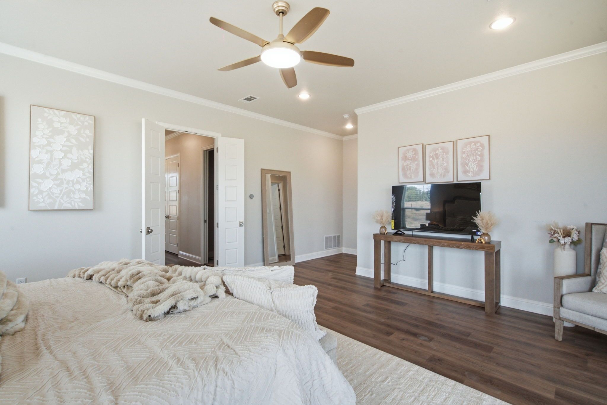 A bedroom with a bed, a ceiling fan, a TV on a wooden stand, and a door leading to another room.