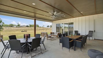 A covered outdoor dining area with a table and chairs, a ceiling fan, and a view of the surrounding landscape.