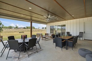 A covered outdoor dining area with a table and chairs, a ceiling fan, and a view of the surrounding landscape.