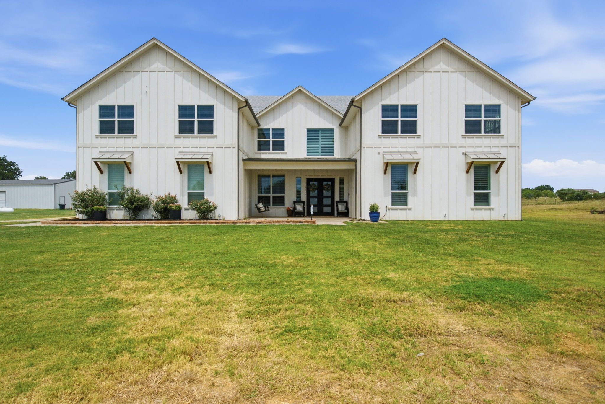 A two-story house with a front porch, large windows, and a well-maintained lawn.