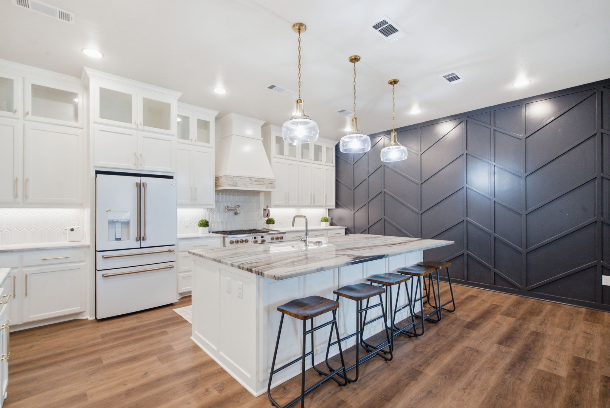A modern kitchen with white cabinetry, a central island with stools, and pendant lighting.