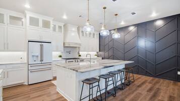 A modern kitchen with white cabinetry, a central island with stools, and pendant lighting.