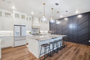 A modern kitchen with white cabinetry, a central island with stools, and pendant lighting.
