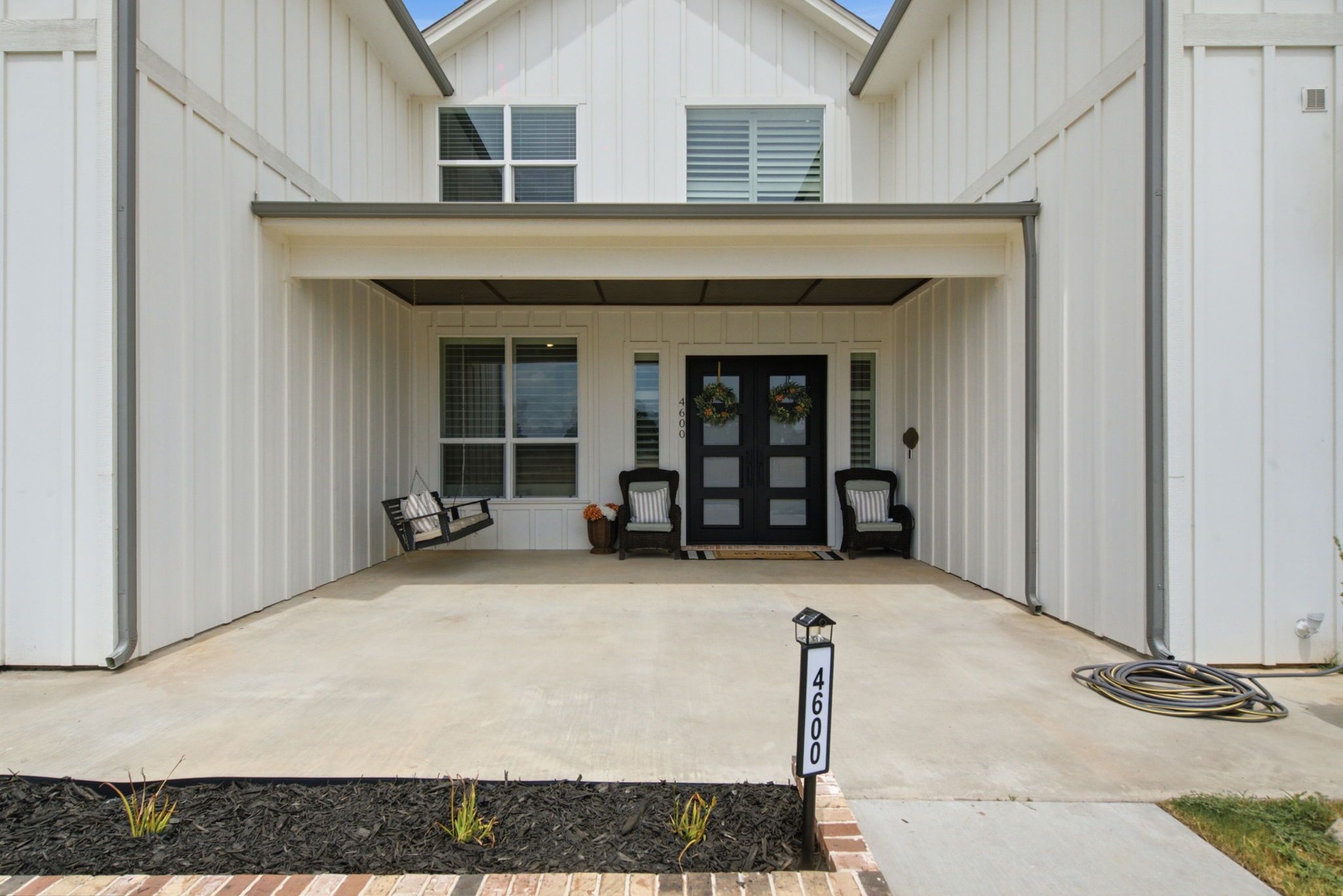 A two-story house with a covered driveway, two front doors, and a mailbox.
