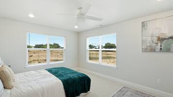 A bedroom with a bed, two windows, a ceiling fan, and a rug.