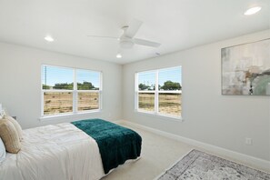 A bedroom with a bed, two windows, a ceiling fan, and a rug.