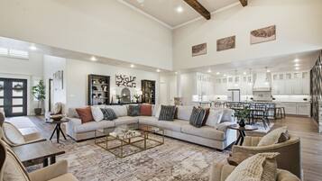 A spacious living area with a large sectional sofa, a coffee table, and a dining area with chairs and a kitchen in the background.