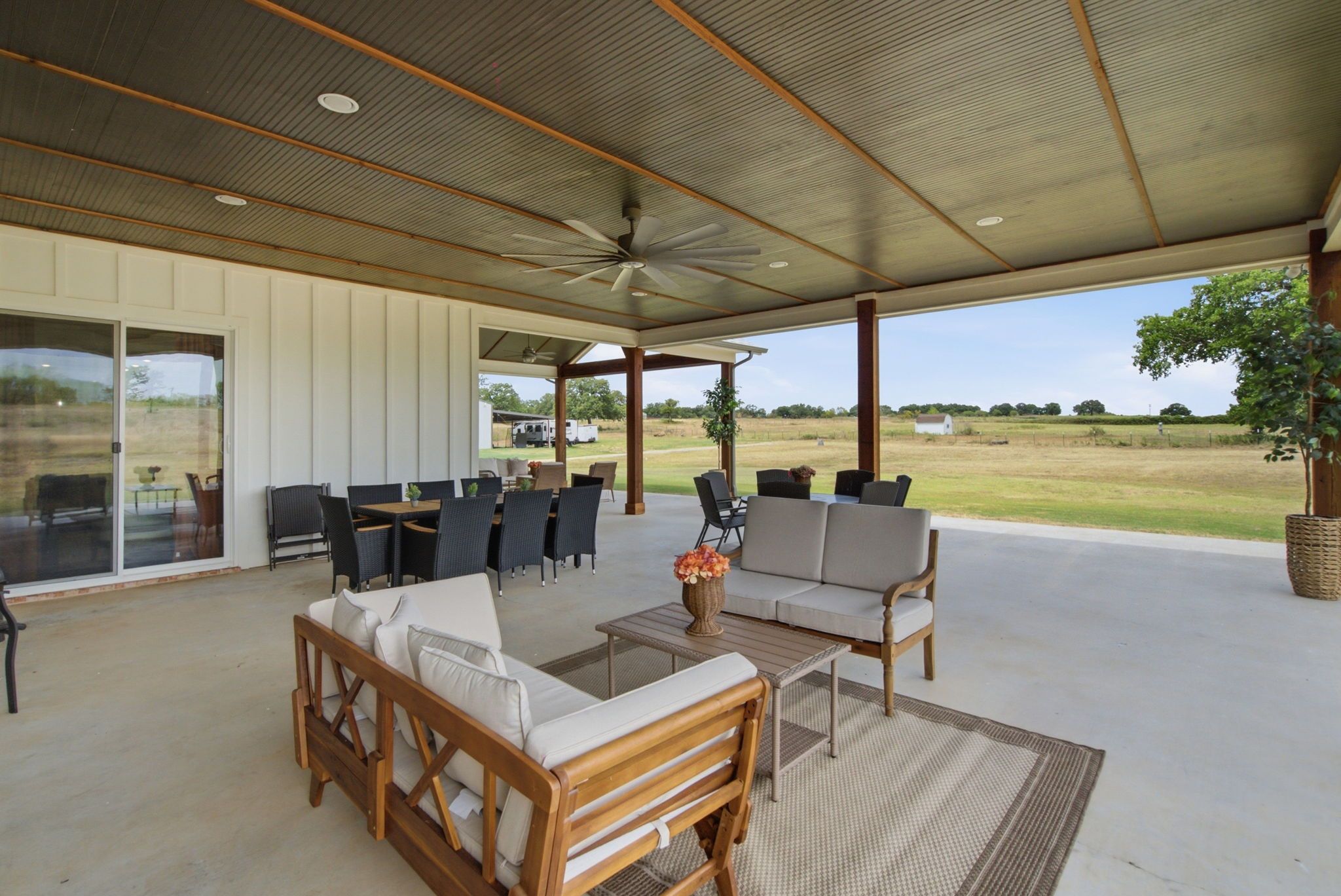 An outdoor covered patio with seating, a ceiling fan, and a view of the countryside.