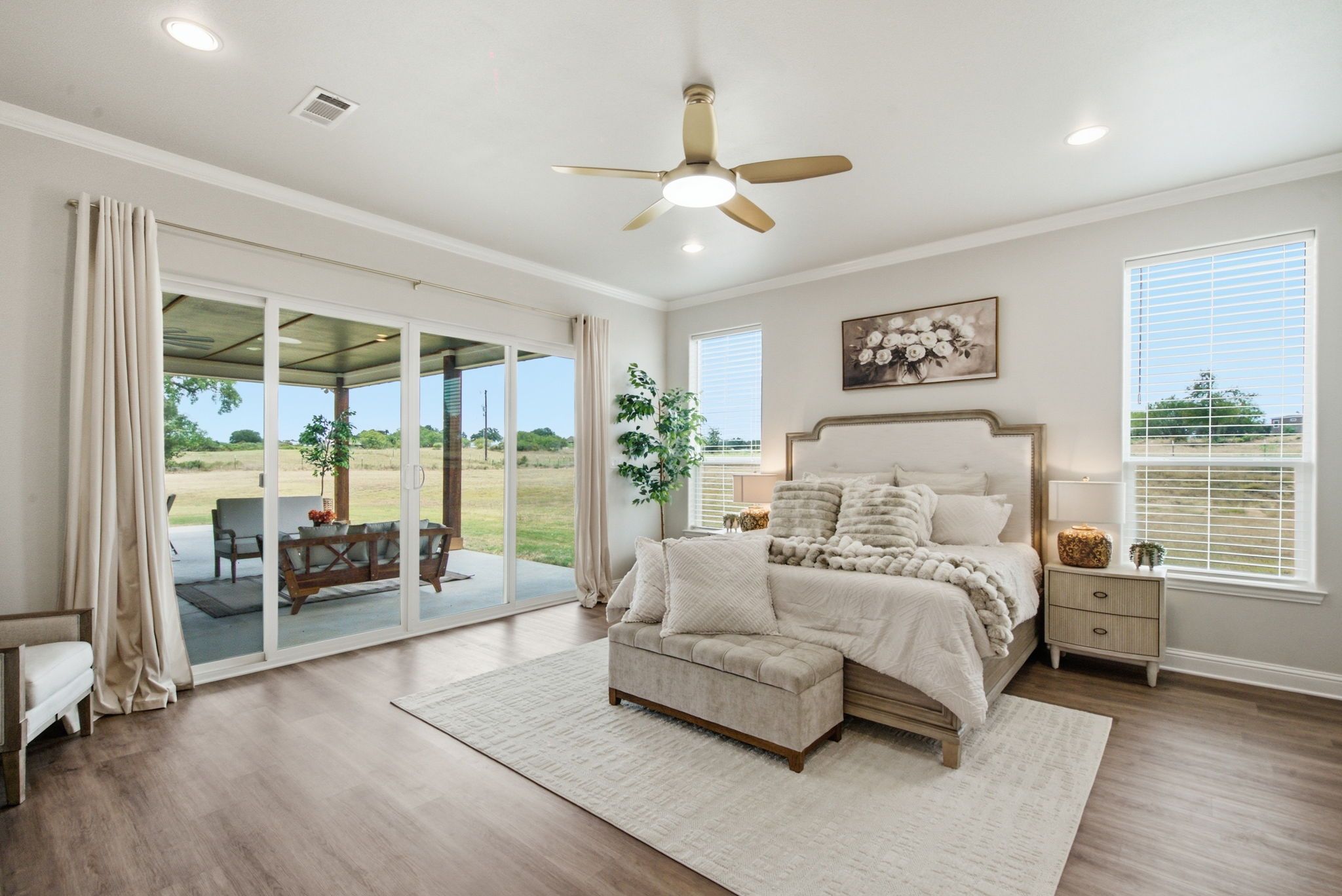 A bedroom with a large bed, a ceiling fan, and a view of the outdoors through sliding glass doors.