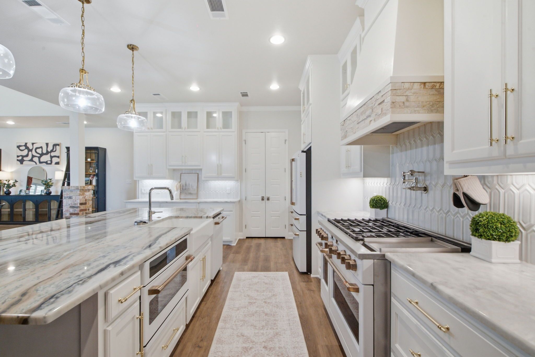 A modern kitchen with white cabinetry, a marble countertop, a gas stove, and a built-in oven.