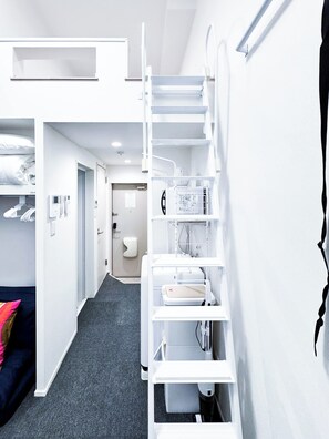Quarto de hotel moderno com beliche, secretária embutida e guarda-roupa branco.