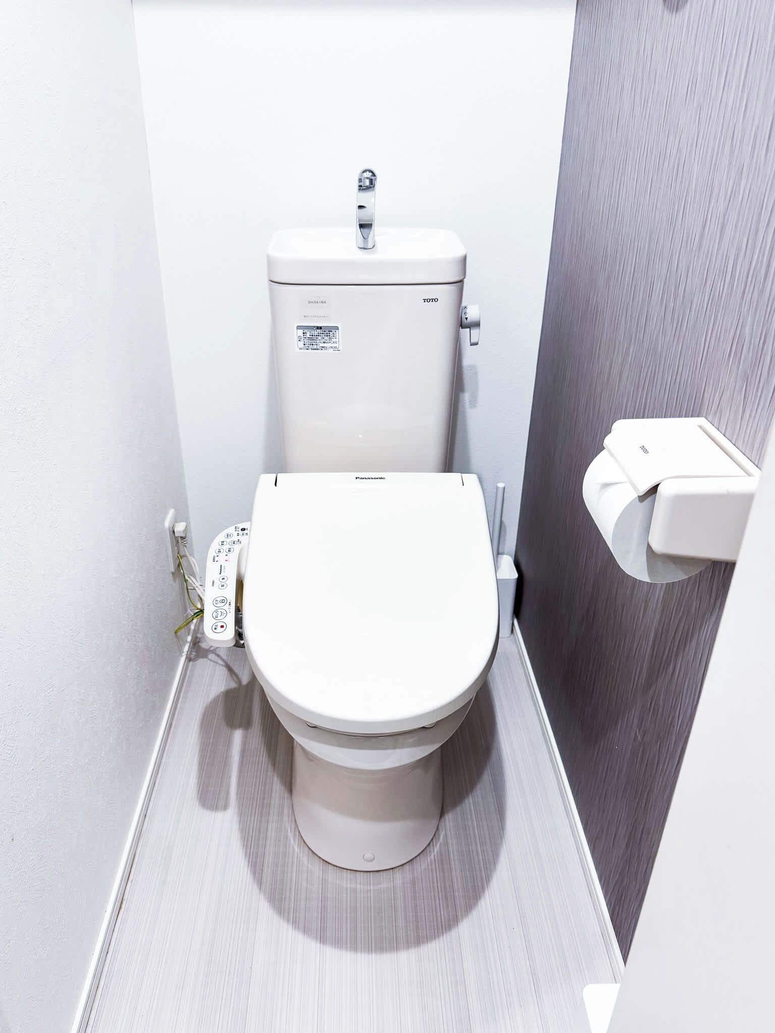 A compact, modern bathroom with a white toilet, a visible control panel, and a wall-mounted bidet.