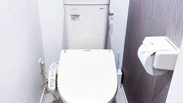 A compact, modern bathroom with a white toilet, a visible control panel, and a wall-mounted bidet.