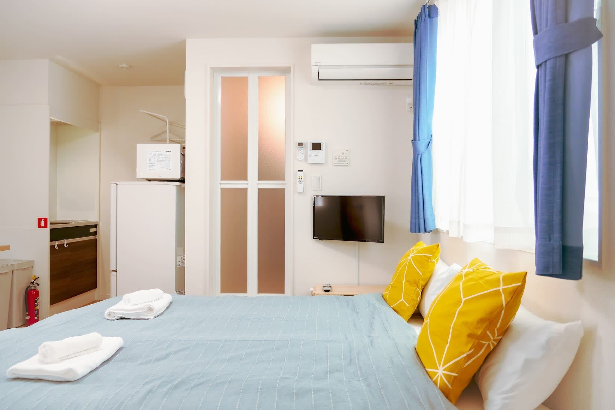 A hotel room with a bed, a flat-screen TV, a kitchenette, and a fire extinguisher.