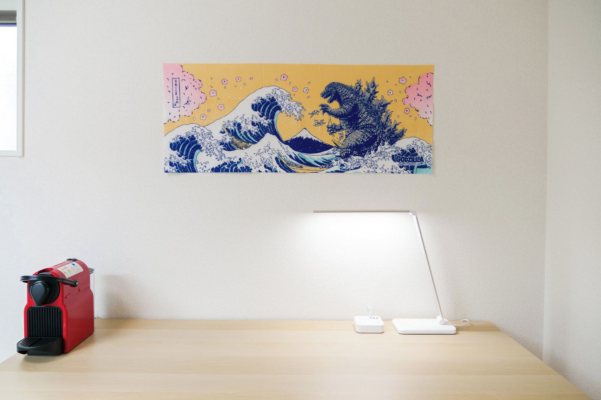 A desk with a red appliance, a white lamp, and a wall-mounted painting.