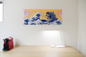 Uma mesa com um eletrodoméstico vermelho, uma luminária branca e um quadro pendurado na parede.