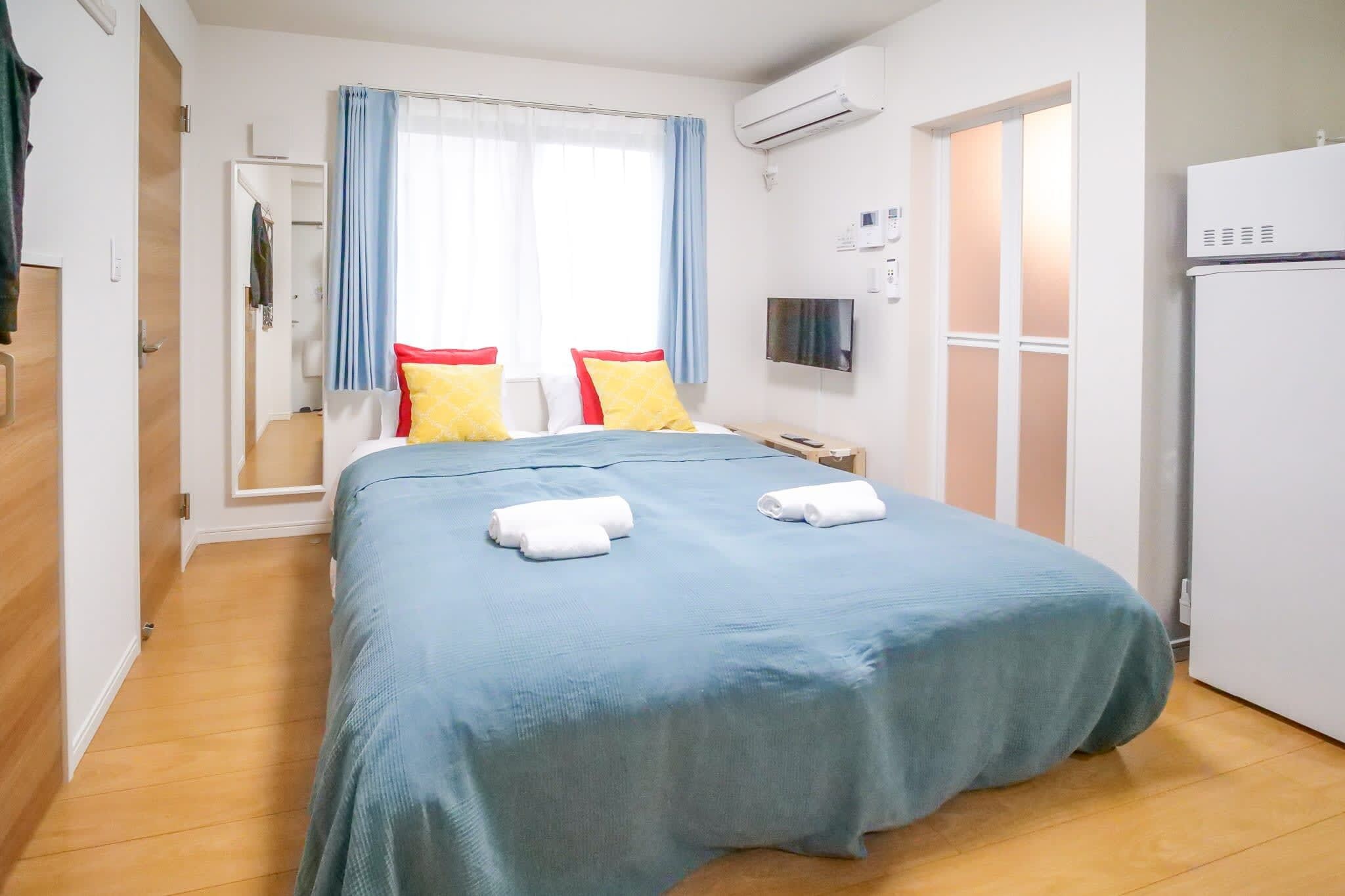 A hotel room with a bed, a TV, an air conditioning unit, and a door.
