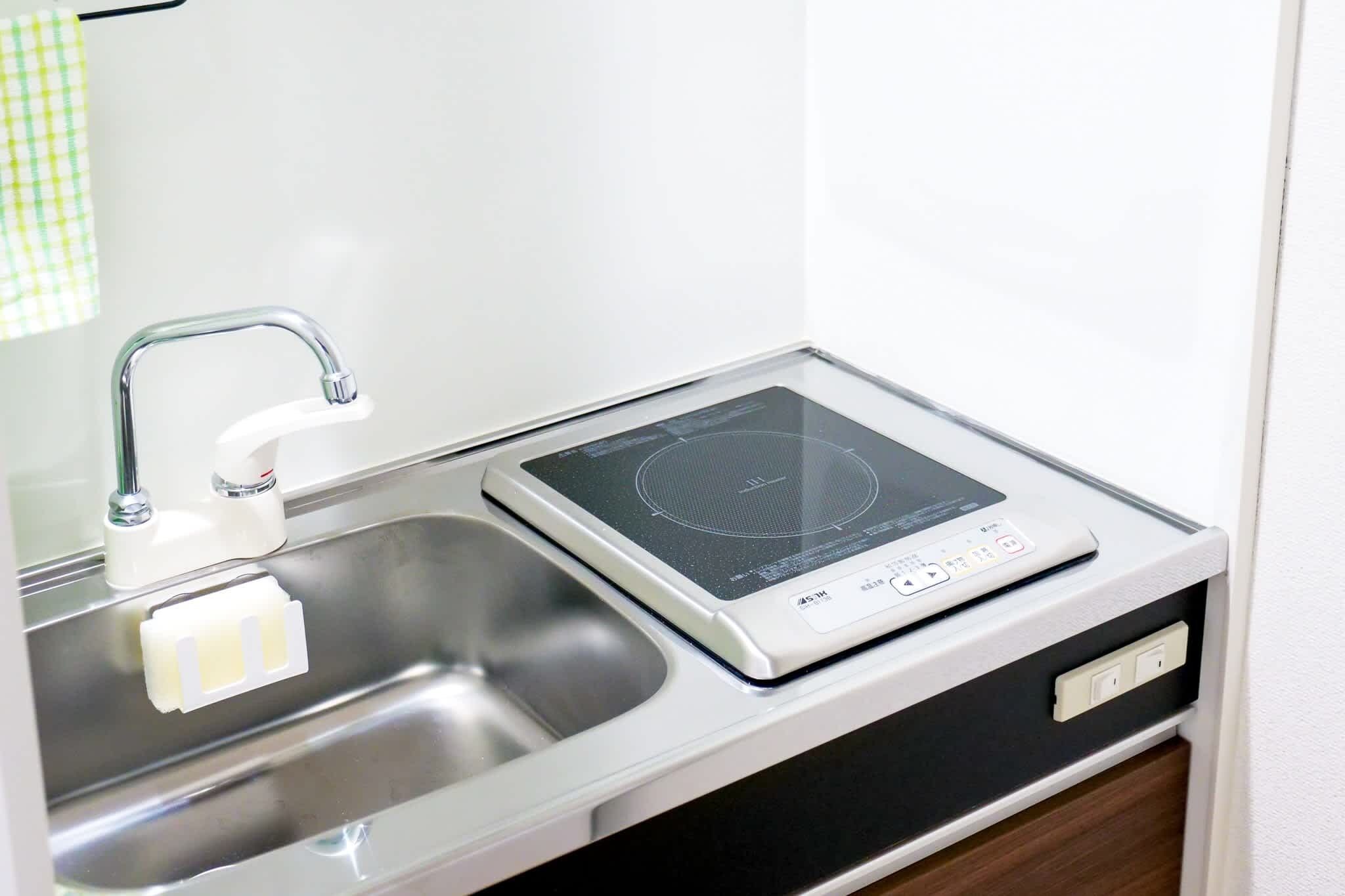A kitchen with a built-in induction cooktop, a stainless steel sink, and a white countertop.