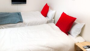 Ein Hotelzimmer mit zwei Betten, jeweils mit weißer Bettwäsche und roten Kissen, einem flachbildfernseher an der Wand und einem Nachttisch aus Holz mit Fernbedienung.
