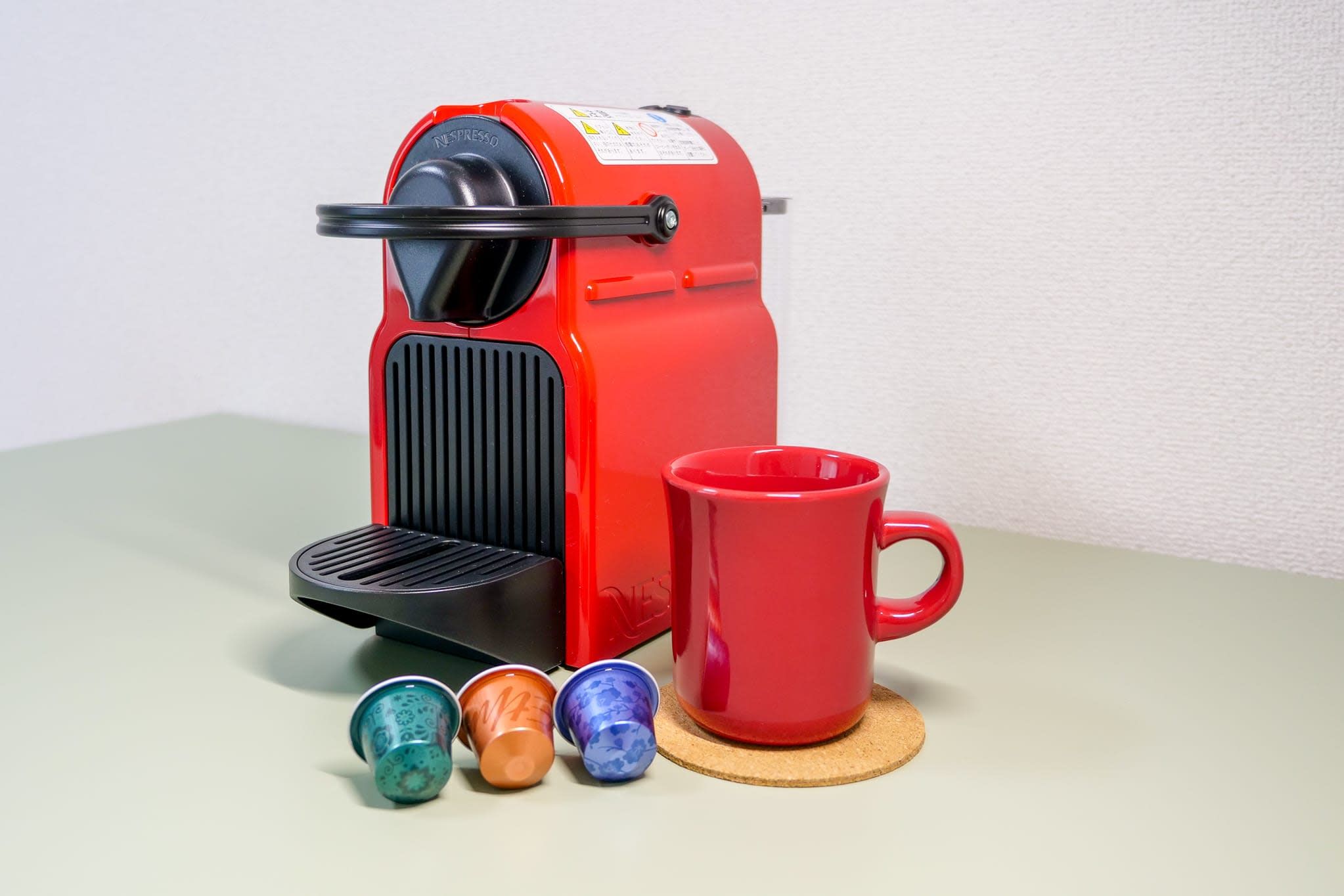 A red Nespresso coffee machine with a red mug and three capsules on a table.