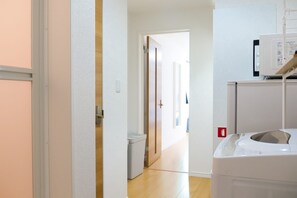 A hallway with a washing machine, a door leading to another room, and a trash bin.