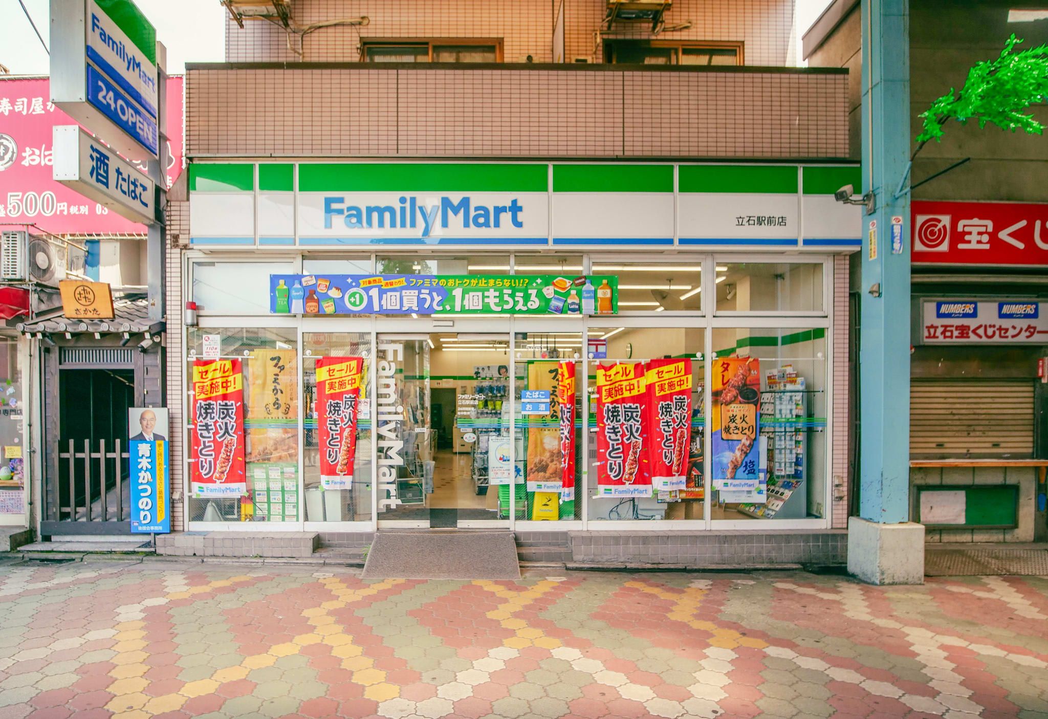 Una tienda FamilyMart con entrada de baldosas, ventanas de vidrio y pancartas promocionales.