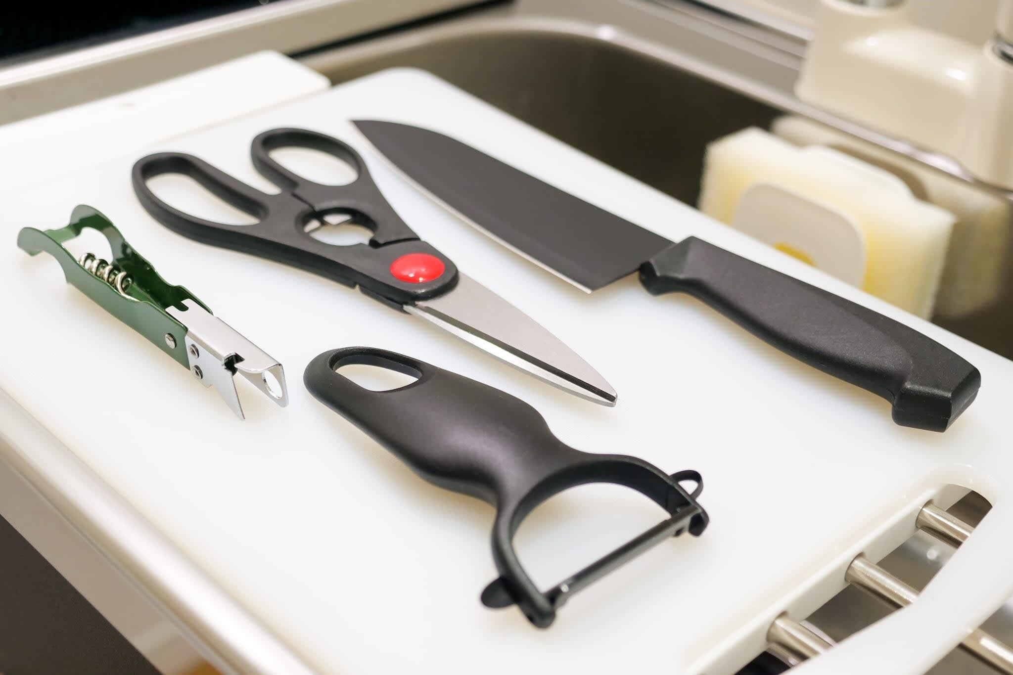 A kitchen drawer with various utensils including scissors, a knife, and a can opener.