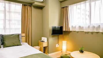 A hotel room with a bed, a bedside table with a lamp, a TV, and a small table with a plant.