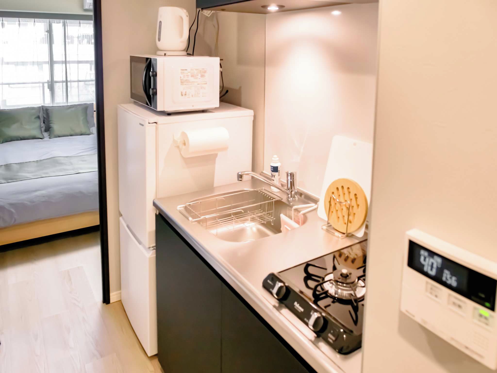 A compact kitchenette with a microwave, a small refrigerator, a sink with a dish rack, and a gas stove.