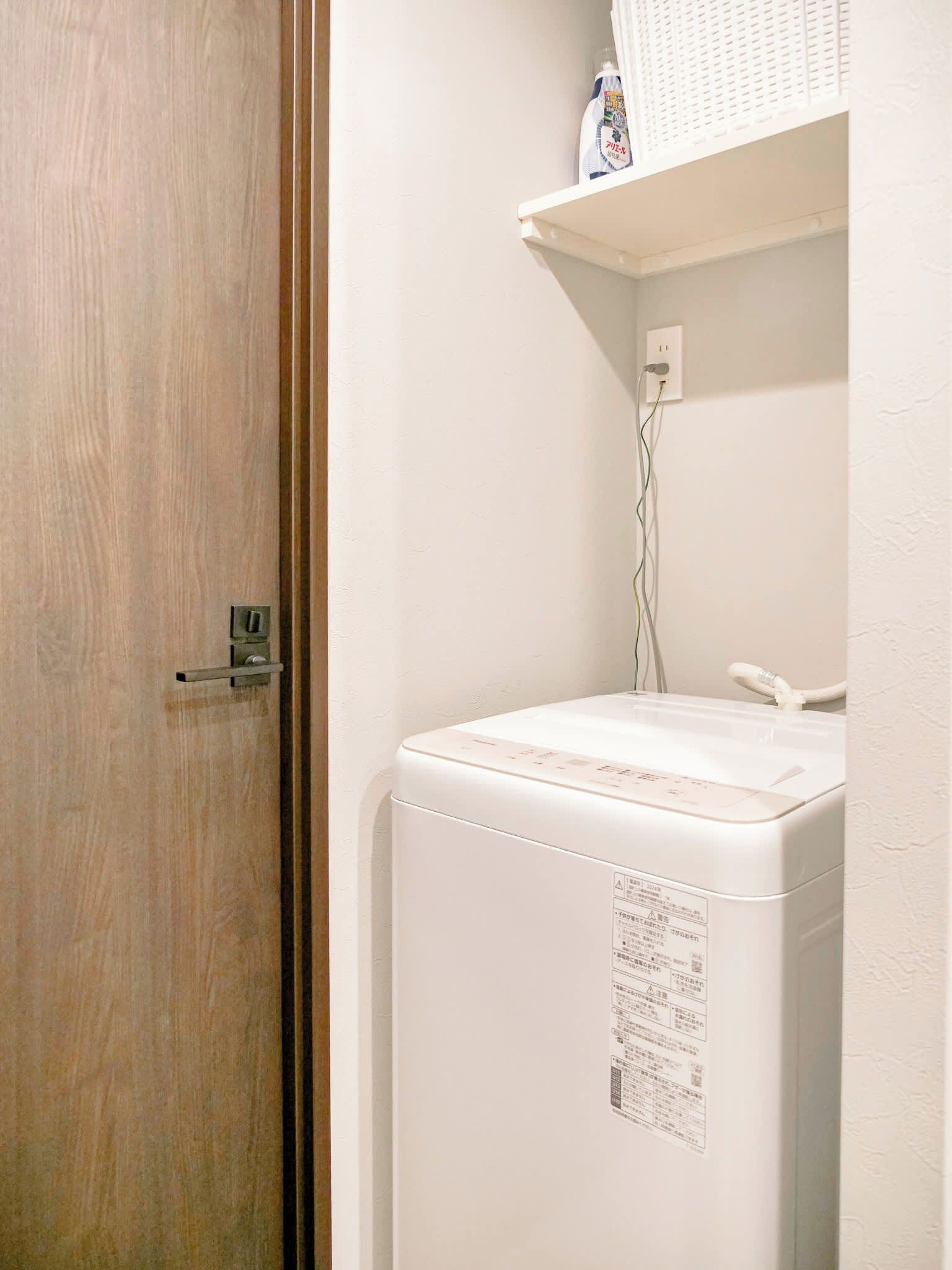 A small laundry room with a white washing machine, a shelf above it, and a door with a handle.