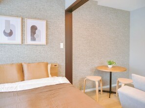 A modern hotel room with a bed, two chairs, a small table with a plant, and two framed artworks on the wall. - Modern Apartment Near JR Nakano Station (Nakano City)
