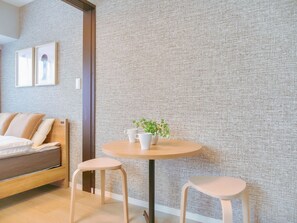 Een moderne kamer met een bed, twee krukken, een ronde tafel met een plant en een gestructureerde wand.