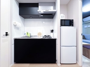 Eine kleine Küche mit schwarzem Arbeitsplatz, einem weißen Kühlschrank, einer Mikrowelle und einem Gasherd.