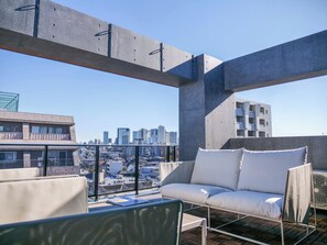 Eine Dachterrasse mit einer Couch und Stühlen, Blick auf die Stadt und einem Betonbau.